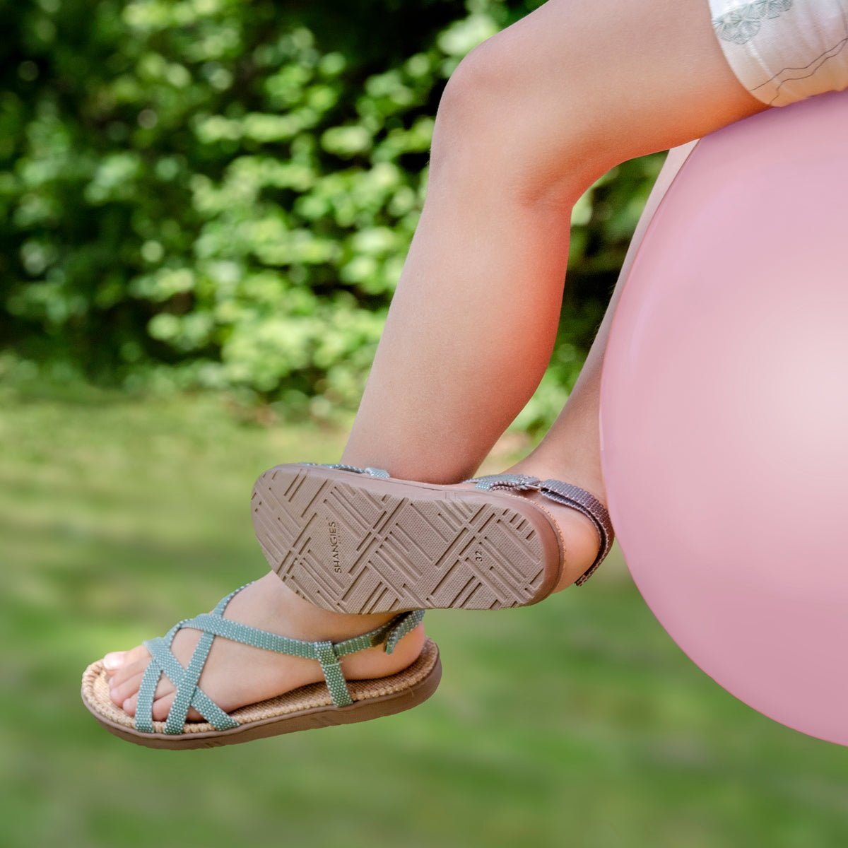 Close-up of Shangies kids sandals in Minty Mint being worn outdoors on grass